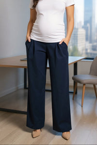 Woman in a white t-shirt and navy pants standing in an office with a cityscape view.