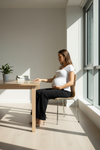 Pregnant woman sitting at a table in a bright room with sunlight streaming in.