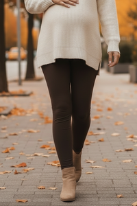 Person wearing a white sweater, black leggings, and brown boots on a sidewalk with autumn leaves.