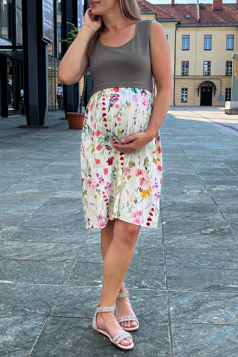 Woman in a floral maternity dress standing on a stone pavement with buildings in the background