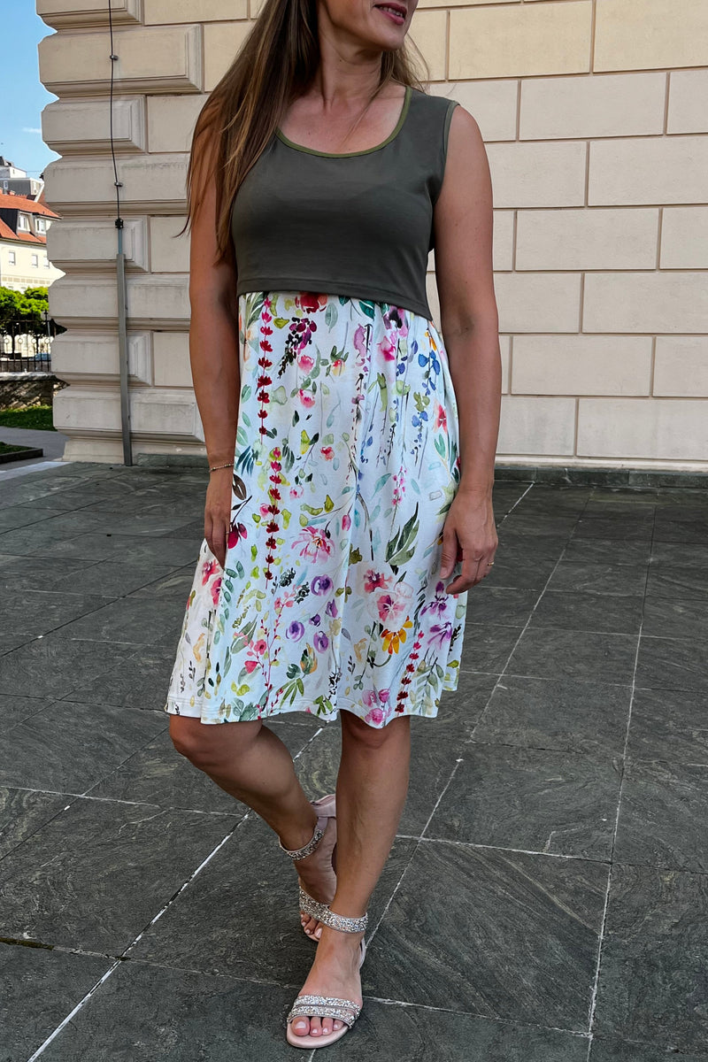 Woman in a floral maternity dress standing on a tiled floor with a building and trees in the background