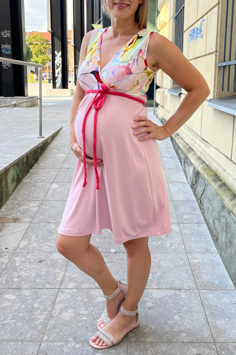 Woman in a pink maternity dress standing on a tiled pavement with a building in the background