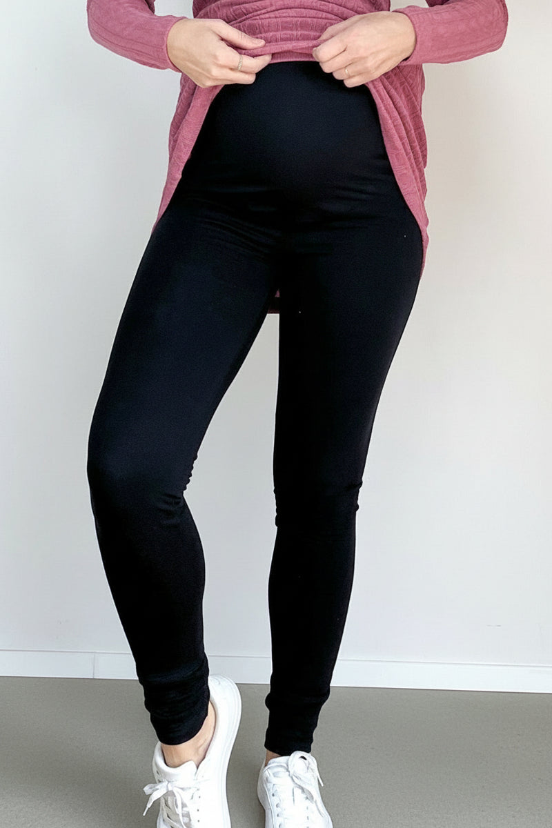 Person wearing black leggings and a pink sweater against a white wall.