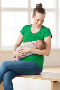 Woman in green shirt breastfeeding a baby on a wooden bench.