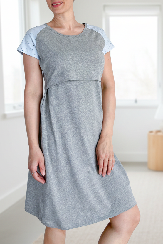 Woman wearing a gray dress standing in a minimalistic bedroom.