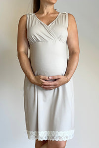 Woman wearing a white sleeveless dress with lace trim, standing against a plain white wall.