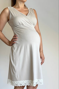 Woman wearing a white dress with lace trim against a plain wall.